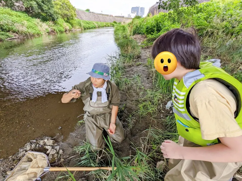 川辺でヘビを見せてもらう子ども
