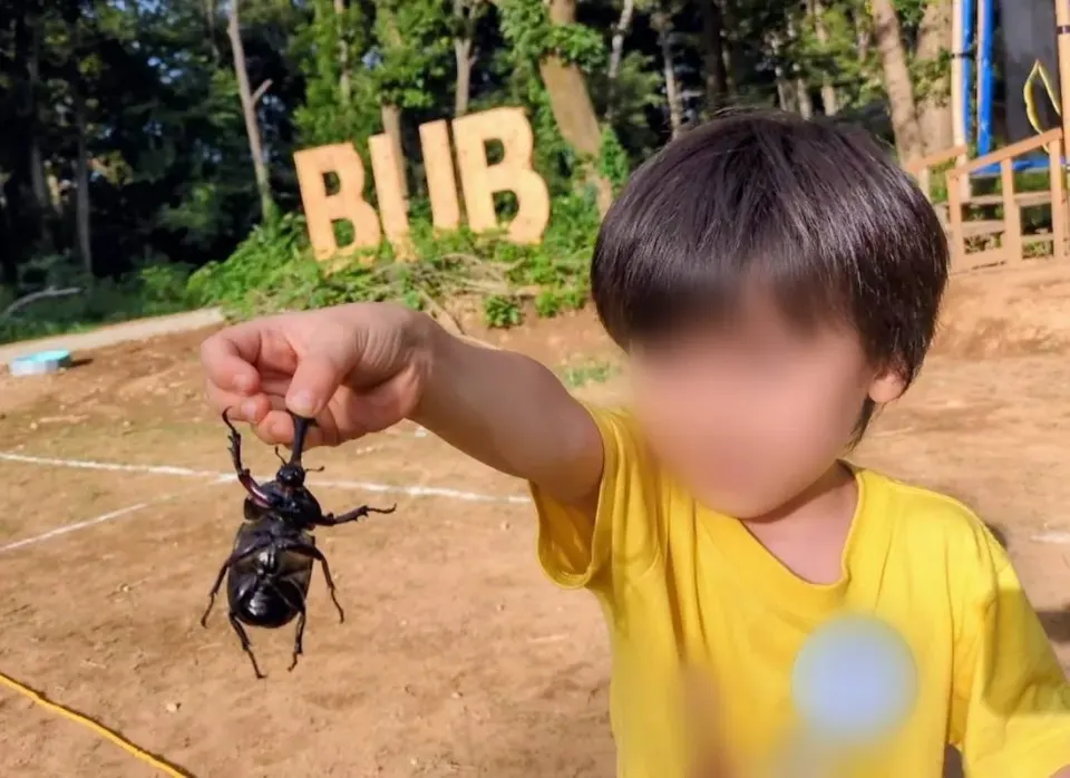 BUBの看板の前で捕まえたカブトムシを持つ子ども